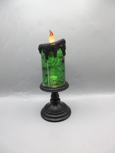 a green candle that is on top of a black stand with a flame in it