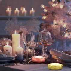 a dining room table set for christmas dinner with candles and plates on it, next to a decorated tree