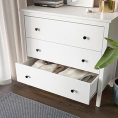 a white dresser with two drawers next to a plant