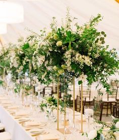 a long table with white flowers and greenery on it is set for an event