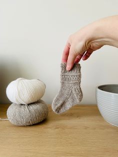 a person is holding a sock next to a ball of yarn on a wooden table