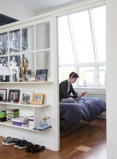 a man sitting on top of a bed in a bedroom next to a book shelf