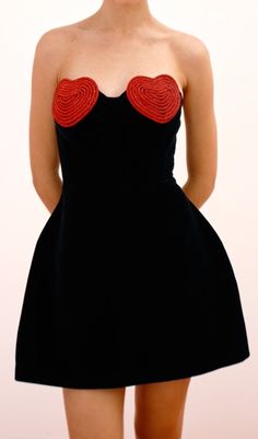 a woman wearing a black dress with red hearts on the chest and under her breast