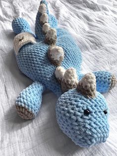 a crocheted blue stuffed animal laying on top of a white bed sheet,