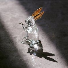 a glass rabbit figurine sitting on top of a table next to a shadow