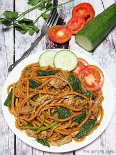 a white plate topped with noodles and veggies next to a cucumber