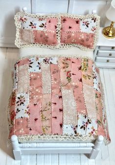 a small bed with pink and white quilts on it's headboard next to a night stand