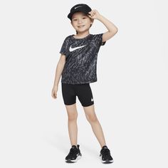 a young boy wearing a black nike shirt and shorts, with his hand on his head