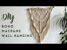 a macrame wall hanging hangs on the wall next to a potted plant