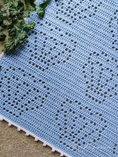 a blue crocheted blanket laying on the ground next to green leaves and flowers