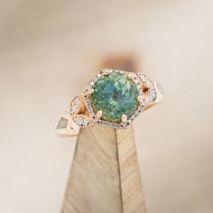 an engagement ring with a green stone surrounded by white and yellow diamonds on top of a wooden stand