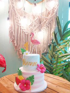 a white cake with pink flowers and flamingos on it sitting on top of a wooden table