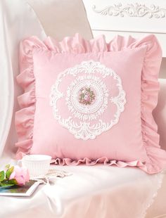 a pink pillow sitting on top of a white couch next to a cup and saucer