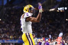 a football player with his hand up in the air and wearing a uniform that says lsu