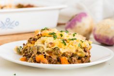 a white plate topped with a casserole covered in cheese and vegetables next to an egg