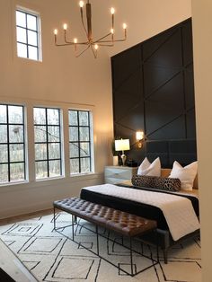 a large bed sitting in the middle of a bedroom next to two windows and a chandelier