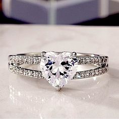 a heart shaped diamond ring on top of a white counter with diamonds surrounding it and the band