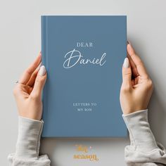 two hands holding a blue book with the title dear daniel written on it, in white lettering