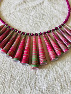 a necklace made out of pink and green paper tubes on a white cloth covered surface