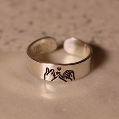 Looking for the perfect promise ring for your best friend or partner? This design features a pinky swear with two human hands, and a tiny heart above, representing the promise the ring creates. Product Details: Materials: Sterling Silver, Fine Silver, or Gold Filled Color: Silver or Gold Size: 6mm You will receive one hand-stamped ring filled with a black enamel finish. Adjustable Heart Ring For Promise And Mother's Day, Adjustable Heart Ring For Promise On Mother's Day, Adjustable Heart Toe Ring For Promise, Adjustable Minimalist Heart Ring For Promise, Adjustable Nickel-free Heart Promise Ring, Adjustable Personalized Rings For Friendship, Personalized Adjustable Rings For Friendship, Personalized Silver Friendship Rings, Personalized Sterling Silver Rings For Friendship