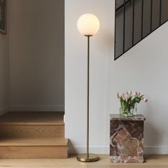 a floor lamp next to a vase with flowers on it and stairs in the background