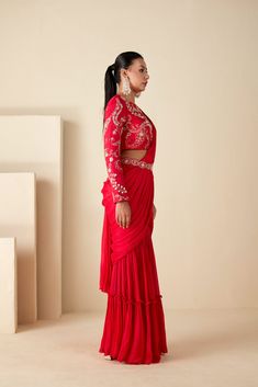 This ensemble features a pre-draped sharara saree in a vibrant red hue, adorned with exquisite craftsmanship. Paired with a beautifully handcrafted blouse, boasting a crew neckline and full sleeves, it exudes sophistication with every detail. The ensemble is accentuated with a separate belt, enhancing its elegance. Crafted from luxurious georgette crepe, both the saree and blouse are meticulously designed for comfort and style, with the blouse lined for added comfort. The back oval cutout adds a touch of allure to this ensemble, making it perfect for special occasions and celebrations. Elevate your ethnic wardrobe with this exquisite ensemble, designed to leave a lasting impression. Blouse And Sharara, Red Sharara, Sharara Saree, Dhoti Saree, Western Gown, Indo Western Gown, Saree And Blouse, Full Sleeve Blouse, Set Saree