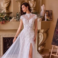 a woman in a white wedding dress standing next to a fireplace with her legs high