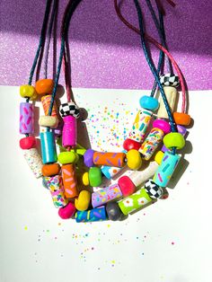 a necklace made out of colorful beads and plastic objects on a purple background with confetti sprinkles