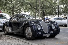 an old black car is parked on the side of the road