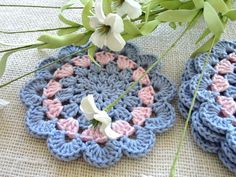 two crocheted coasters sitting on top of a table next to a plant