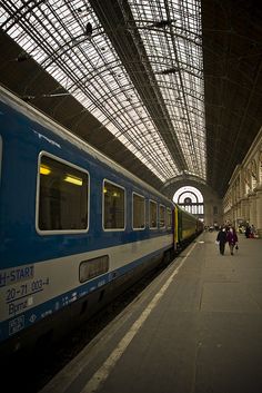 people are walking on the platform next to a blue and white train in a station