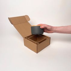 a person holding a coffee cup in a cardboard box with the lid open to reveal it's inner compartment