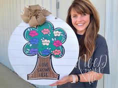 a woman holding up a sign that says love grows here with a tree on it