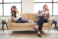 a man and woman sitting on a couch talking on their cell phones in an office