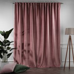 a living room with a pink curtain and green pillows on the floor next to a lamp