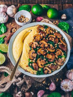 a bowl filled with mushrooms and spinach on top of a wooden table next to garlic,