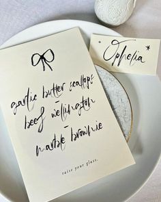 two pieces of paper with writing on them sitting on a plate next to a salt shaker