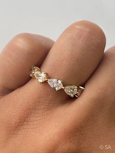 a woman's hand with a gold ring on top of her finger and three pear shaped diamonds in the middle