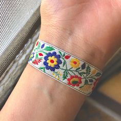 a woman's hand with a white wristband decorated with colorful flowers