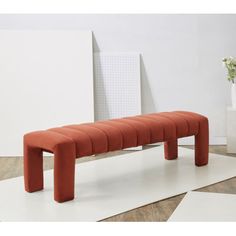 an orange bench sitting on top of a white floor next to a vase with flowers