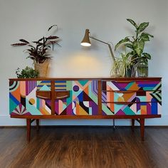 a colorful sideboard with potted plants on top and a lamp above it in an empty room