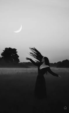 a woman with her hair blowing in the wind at dusk, near a crescent moon