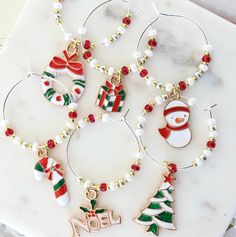 four christmas themed wine charms on a marble table with white and red beads around them