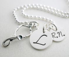 "RN Graduation Necklace Gift - Personalized Nurse Necklace RN Graduation Custom Jewelry Hand Stamped Sterling Silver Custom Nurse Necklace The 1/2\" sterling silver disc is hand stamped with the initial of your choice. The 3/8\" disc is hand stamped with the abbreviation \"R.N.\". Hanging with the name charms is a sterling silver stethoscope charm. This necklace comes on an 18\" sterling silver bead chain. If you would like to inquire about other chain options, please convo us prior to placing y Hand Stamped Sterling Silver Round Pendant Necklace, Sterling Silver Hand Stamped Round Disc Necklace, Sterling Silver Dog Tag Necklace With Charms, Adjustable Hand Stamped Silver Necklace, Sterling Silver Pendant Jewelry, Silver Dog Tag Jewelry With Charms, Stamped Sterling Silver Round Disc Charm Necklace, Sterling Silver Stamped Round Disc Charm Necklace, Silver Stamped Dog Tag Necklace