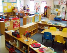 a classroom filled with lots of wooden desks and bookshelves covered in children's artwork