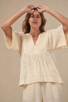 The Tulum top from Australian brand Little Lies is a perfect staple for spring/summer. Features pleated detail on the front, a flattering square sleeve and a v-neckline. This gorgeous top is an oversized fit that can be paired with your favorite pants or shorts. Semi-sheer. Materials: 100% Cotton Care: Wash with like colors; cold gentle machine wash; do not bleach; lay flat to dry; warm iron; do not tumble dry. Size Info: Model is 5'8" and is wearing a size S; relaxed fit Size Guide | Shipping Policy Versatile V-neck Blouse For Beach, Relaxed V-neck Blouse For Day Out, Beige V-neck Summer Top, Versatile Beige V-neck Blouse, Beige V-neck Top For Summer, Effortless V-neck Blouse For Day Out, Casual Cream V-neck Top, Chic Short Sleeve V-neck Top For Spring, Versatile Beige V-neck Top