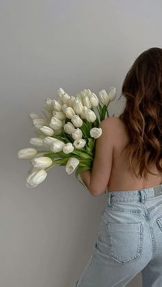 a woman holding a bunch of white tulips in her right hand and back to the camera