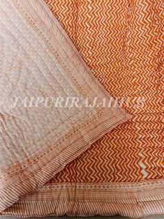 an orange and white quilted bed spread on top of a wooden floor next to two pillows