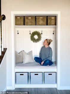 a woman sitting on top of a bench next to some bins and drawers in a room