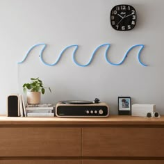 a record player sitting on top of a wooden dresser next to a clock and plant